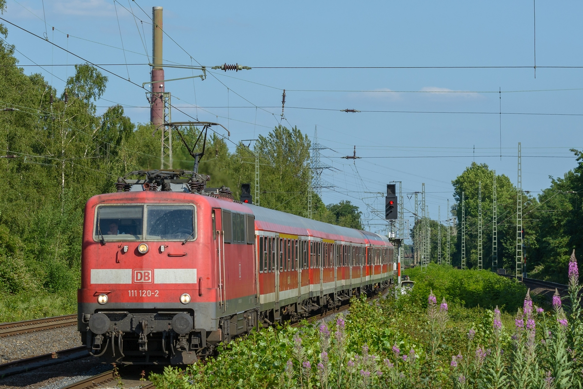 Die schon arg verwitterte 111 120-2 fährt am 06.07.2015 mit einem HVZ-Verstärkerzug in den Bahnhof von Dinslaken ein.