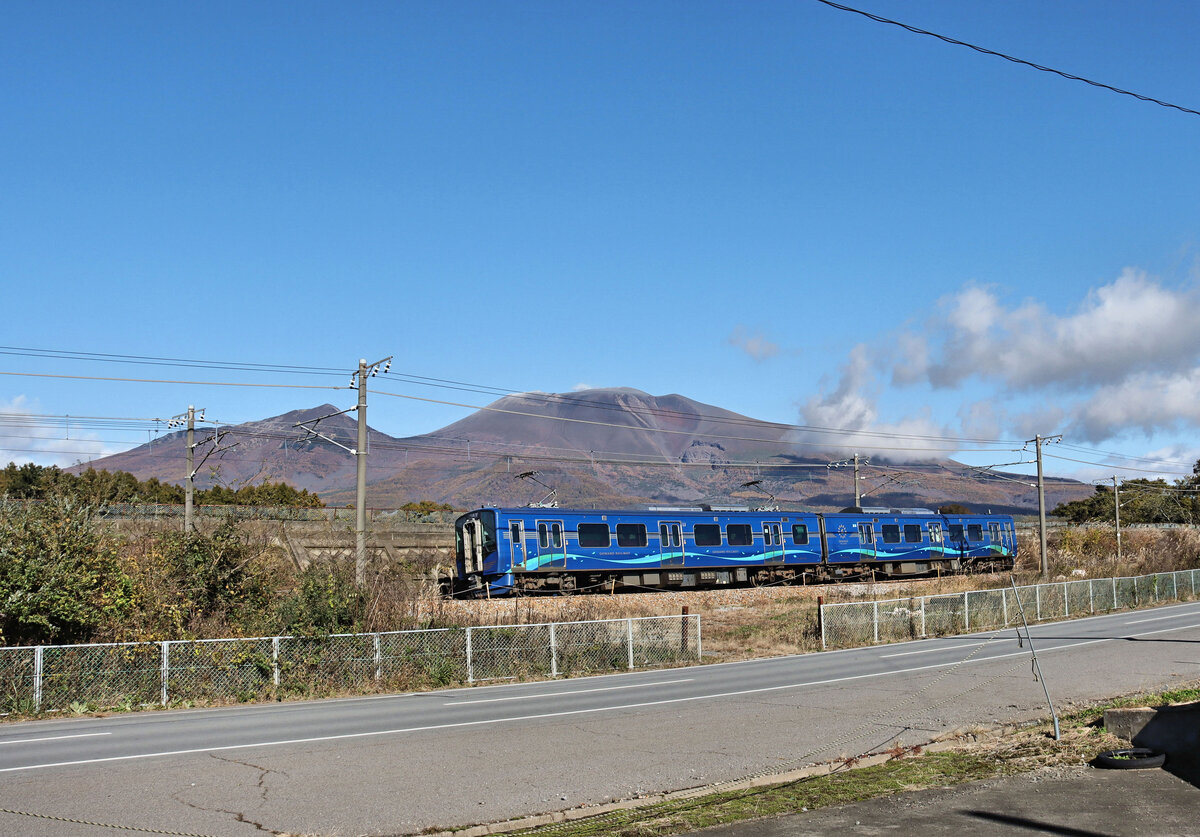 Die Shinano-Bahn (I): Shinano ist der alte Name der heutigen Praefektur Nagano, mitten in den zentralen japanischen Bergen, ohne Zugang zum Meer. Die Shinano-Bahn begann ihren Betrieb am 1.Oktober 1997, am Tag der Er�ffnung der neuen Shinkansen (Hochgeschwindigkeits)-Strecke von Tokyo nach Nagano, wo von 7.Februar 1998 bis 22.Februar 1998 die Olympischen Winterspiele stattfanden. Dabei wurde die einst als Zahnradbahn gebaute (sp�ter auf Adh�sionsbetrieb mit Schiebe- bzw.Bremslokomotiven umgebaute) ber�hmte Usui-Rampe nach Karuizawa in der Hochebene hinauf stillgelegt. Der Lokalverkehr ab Karuizawa wurde dann von der JR abgestossen und ging an die neu gegr�ndete Shinano-Bahn �ber. Expressz�ge brauchte es nicht mehr, seit die Hochgeschwindigkeitsbahn eingeweiht wurde. Die Strecke von Karuizawa hinunter zum Talboden in Nagano ist 74, 4 km lang, davon bef�hrt die Shinano-Bahn 9, 3 km einer einm�ndenden JR-Strecke. Im Bild f�hrt Zug S101 am Fusse des aktiven Vulkans Asama nach Shinano Oiwake und Karuizawa hinauf. 7.November 2024 