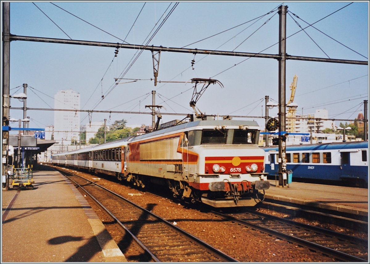 Die SNCF CC 6558 wartet in Dijon mit einem Reisezug auf die Abfahrt, wahrscheinlich in Richtung Lyon. Die von der SNCF 1969 bis 1975 beschafften Gleichstromloks waren im hochwertigen Reiseverkehr, insbesondere im innerfranzösischen TEE Verkehr Paris - Bordeaux/Toulouse/Marseille eingesetzt. 
Die letzte der 200 km/h schnellen Lok wurde 2007 aus dem Dienst genommen. 

Analogbild / September 1998