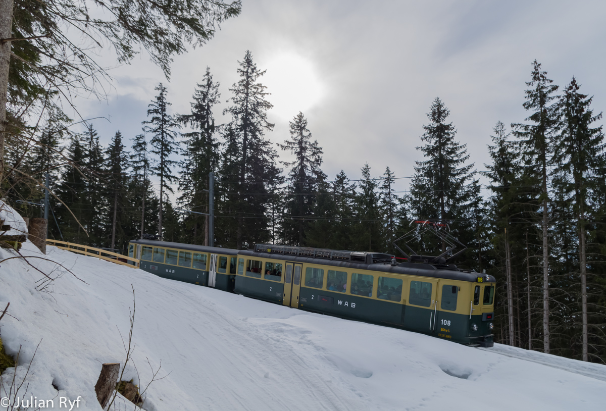 Die Sonne versteckte sich am 15. März 2015 leider lange Zeit hinter dünnen Schleierwolken, was für dieses Bild aber von Vorteil war. Der BDhe 4/4 108 der WAB fährt mit seinem Skizug oberhalb der Allmend talwärts Richtung Wengen.