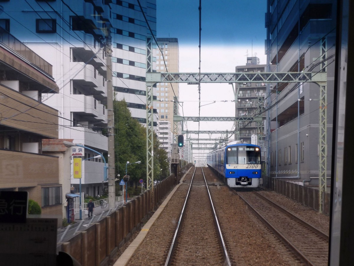 Die Stammstrecke des Keihin Kyûkô (Keikyû)-Konzerns: Die dichte Bebauung und engen Platzverhältnisse entlang der Keikyû-Strecke zwischen Tokyo und Yokohama geben oft eine düstere und bedrückende Stimmung. Hier kommt der blaue Zug 2157 (Serie 2100) auf einer Direktverbindung zwischen den beiden internationalen Flughäfen von Tokyo entgegen. Hatchô Nawate in der Stadt Kawasaki, 24.Oktober 2011.  