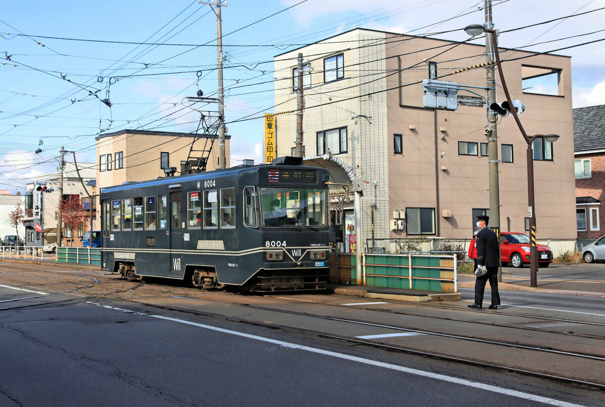 Die Strassenbahn von Hakodate (Japan, Süd-Hokkaidô): Wagen 8004 (1993 durch Umbau entstanden) vor dem Betriebshof Komaba Shako am 30.Oktober 2022. Ein wie immer sehr korrekt angezogener Fahrer geht den Wagen übernehmen. 