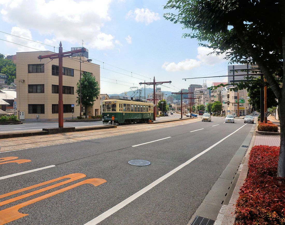 Die Strassenbahn von Nagasaki - Das Rollmaterial: Wagen 211-216. Als Nachbau zu den Wagen 201-210 erschienen diese Wagen 1951. Um 1985 modernisiert und klimatisiert. Im Bild Wagen 213 beim Abstieg von Hotaru Jaya auf der nördlichen der drei Linien in die Berge hinein. Man sieht hier gut die typische Konfiguration, die auch bei der Erneuerung japanischer Strassenbahnen beibehalten wird: Die Bahn fährt in der Strassenmitte, und Fahrgäste müssen Ewigkeiten warten, bis die endlosen Autokolonnen endlich Rot bekommen, damit man die Strasse zur Haltestelle überqueren kann (meist ist dann die Strassenbahn schon abgefahren). Oder man geht - wie vorne in der Distanz erkennbar - gleich über eine Passerelle zur Haltestelle. 8.August 2013.  