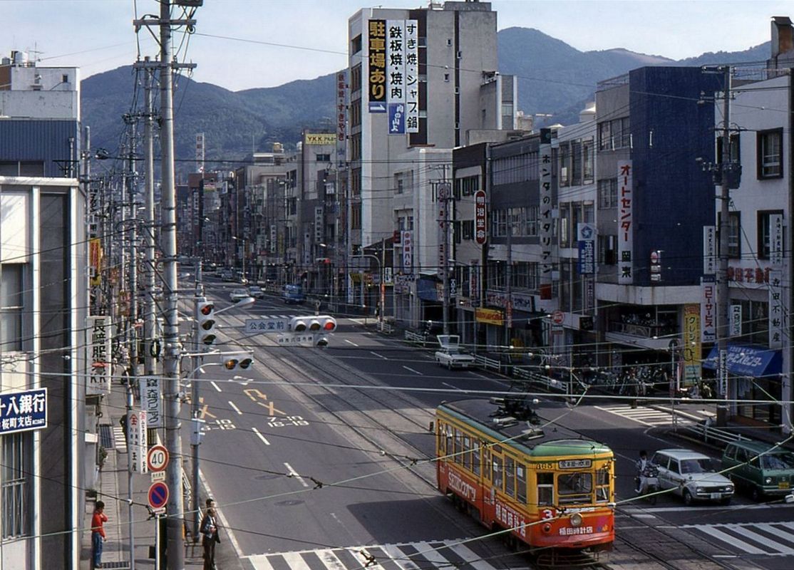 Die Strassenbahn von Nagasaki - Wagen 365 (Serie 361-367) in der Innenstadt am 20.März 1981. Erst ein einzelnes richtiges Hochhaus ist zu sehen, und darauf prangt grosse Werbung für die darin befindlichen Restaurants mit Speisen aus gebratenem Fleisch. 