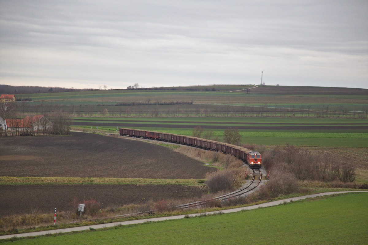 Die Strecke zwischen Mistelbach und Hohenau folgt weitgehend der Zaya, ohne sie jemals zu queren. Dadurch ergibt sich gerade zwischen Prinzendorf-Ranersdorf und Hauskirchen ein sehr kurviger Streckenverlauf, wie hier im Bild zu sehen ist.
Das triste Wetter passt gut zur Stimmung, ist dies doch der letzte Zug auf dieser Strecke. (12.12.2015)
