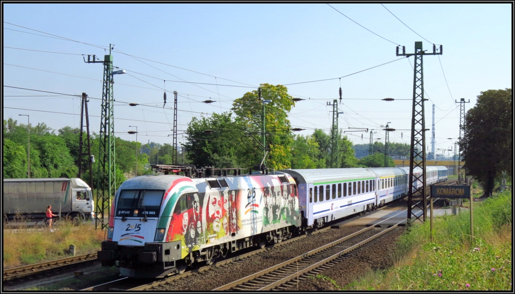 Die Taurus 470 003 der MAV im  25 Jahre deutsch-ungarische Freundschaft Design  ist mit dem Warschau Express am Haken aus Budapest unterwegs in Richtung Györ. Hier zu sehen am Stadtrand von Komárom (H) am 06.August 2015.