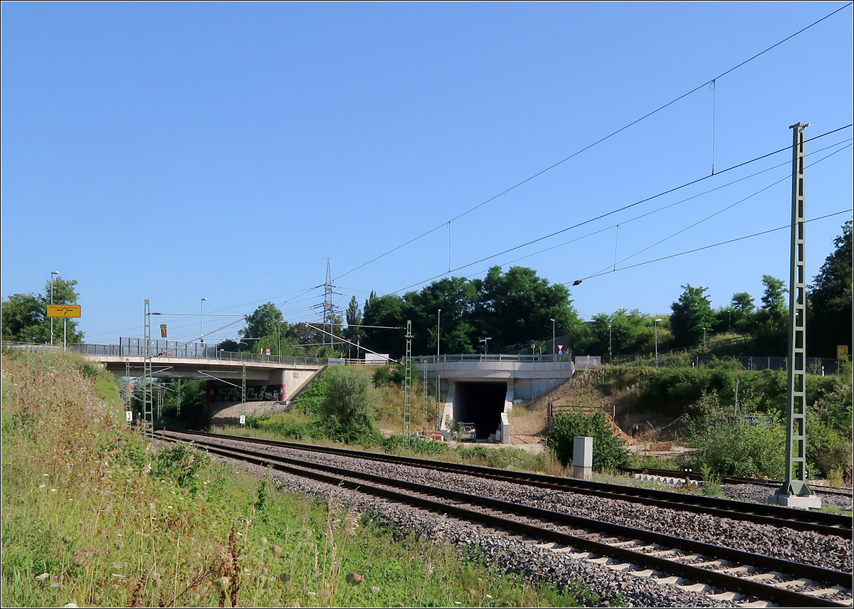 Die Wendlinger Kurve - 

Um Züge aus Richtung Tübingen in Richtung Stuttgart an die Neubaustrecke anzuschließen entsteht zwischen Ober- und Unterbohingen eine weitere Verbindungskurve von der Neckar-Alb-Bahn. Zunächst sollte diese auch nur eingleisig angelegt werden (Kleine Wendlinger Kurve), doch wurde dann auch der Bau des zweiten Gleises vorgezogen. 

Im Bild das Tunnelportal kurz nach dem Abzweig von der Neckar-Alb-Bahn. Hier wird schon an der bahntechnischen Ausrüstung gearbeitet. Dieser Tunnel ist Teil der kleinen Wendlinger Kurve, das zukünftige Streckengleis von der Neubaustrecke in Richtung Tübingen. Von Rohbauarbeiten für das Gleis der Gegenrichtung, das rechts daneben in einem weiteren Tunnel verschwinden wird ist an dieser Stelle noch gar nichts zu sehen.

14.08.2021 (M)