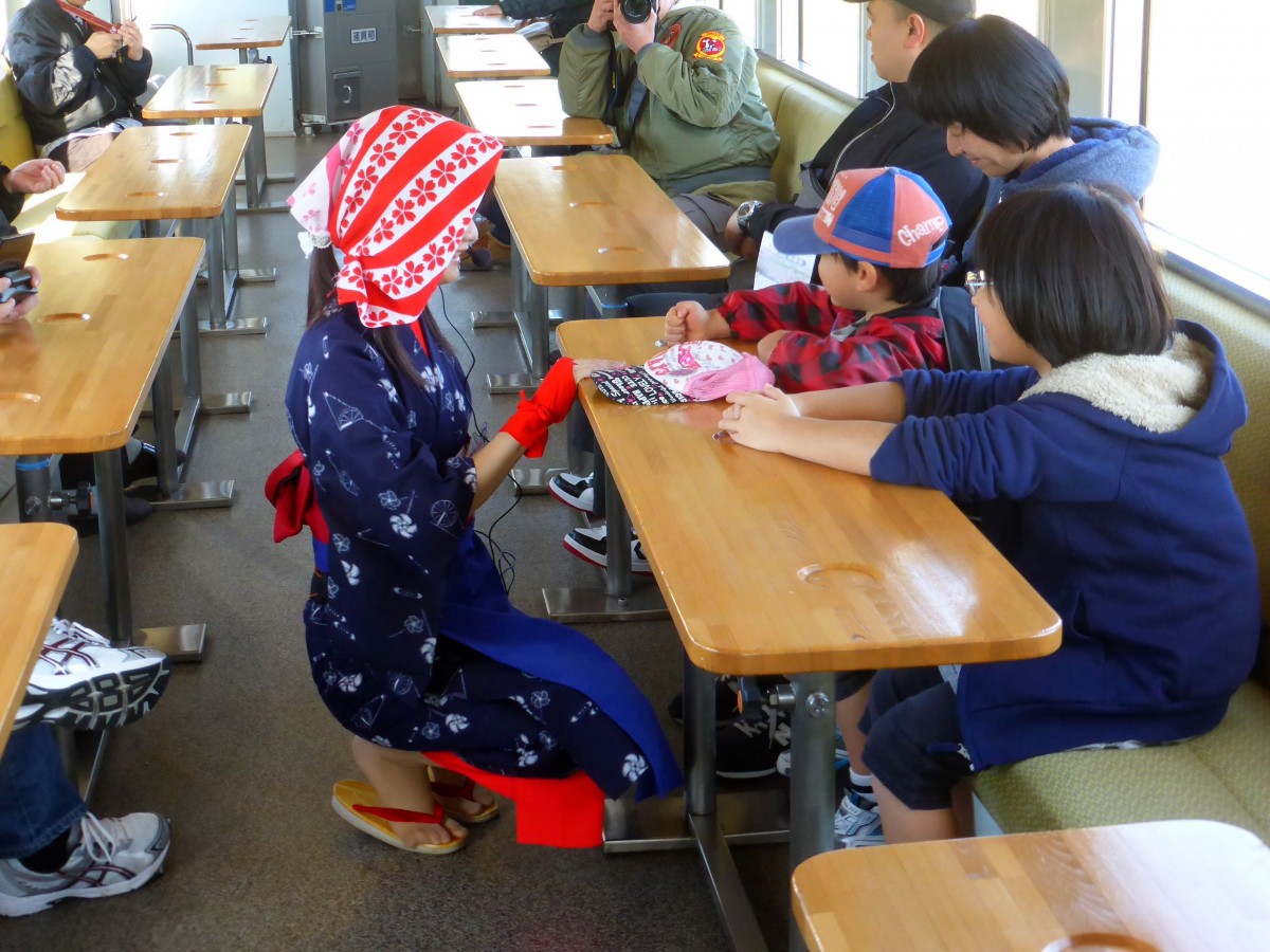 Die Yuri Kôgen-Bahn: Auf einigen Kursen fährt eine Zugbegleiterin mit, die dafür sorgt, dass sich die Fahrgäste wohlfühlen; zugleich wirbt sie für die Attraktionen dieser doch recht abgelegenen Gegend. Selbstverständlich hält sie sich an die Regel, dass man Kinder in Japan grundsätzlich nie von oben herab anspricht, sondern stets auf Augenhöhe. In Wagen 2002, 2.November 2013.  