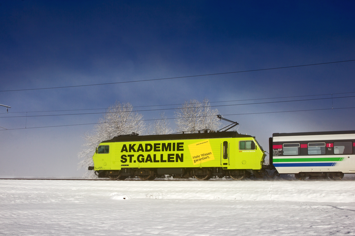 Die Zuglok Re 446 018  Akademie St.Gallen  fährt unter einem leicht ausgebildeten Nebelbogen mit dem VAE vorüber.Bild vom 24.2.2016