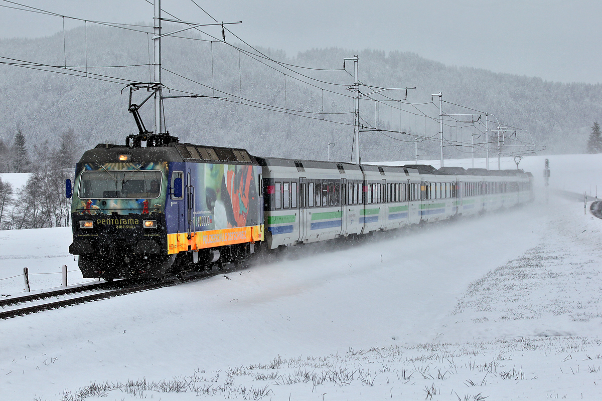 Die Zuglokomotive Re 456 092 Amriswil wirbelt eine Menge Schneestaub auf als sie mit dem Voralpenexpress bei Altmatt vorbeibraust.Bild vom 11.1.2015