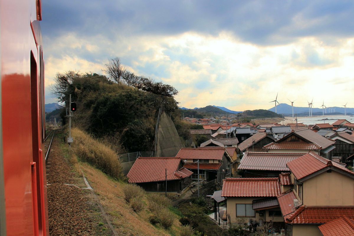 Dieselzüge von JR-Westjapan an der Küste des Japanischen Meeres: Blick aus dem Triebwagen KIHA 47 2018 über die Dachlandschaft und die Meeresküste von Kuromatsu. 26.März 2017. 
