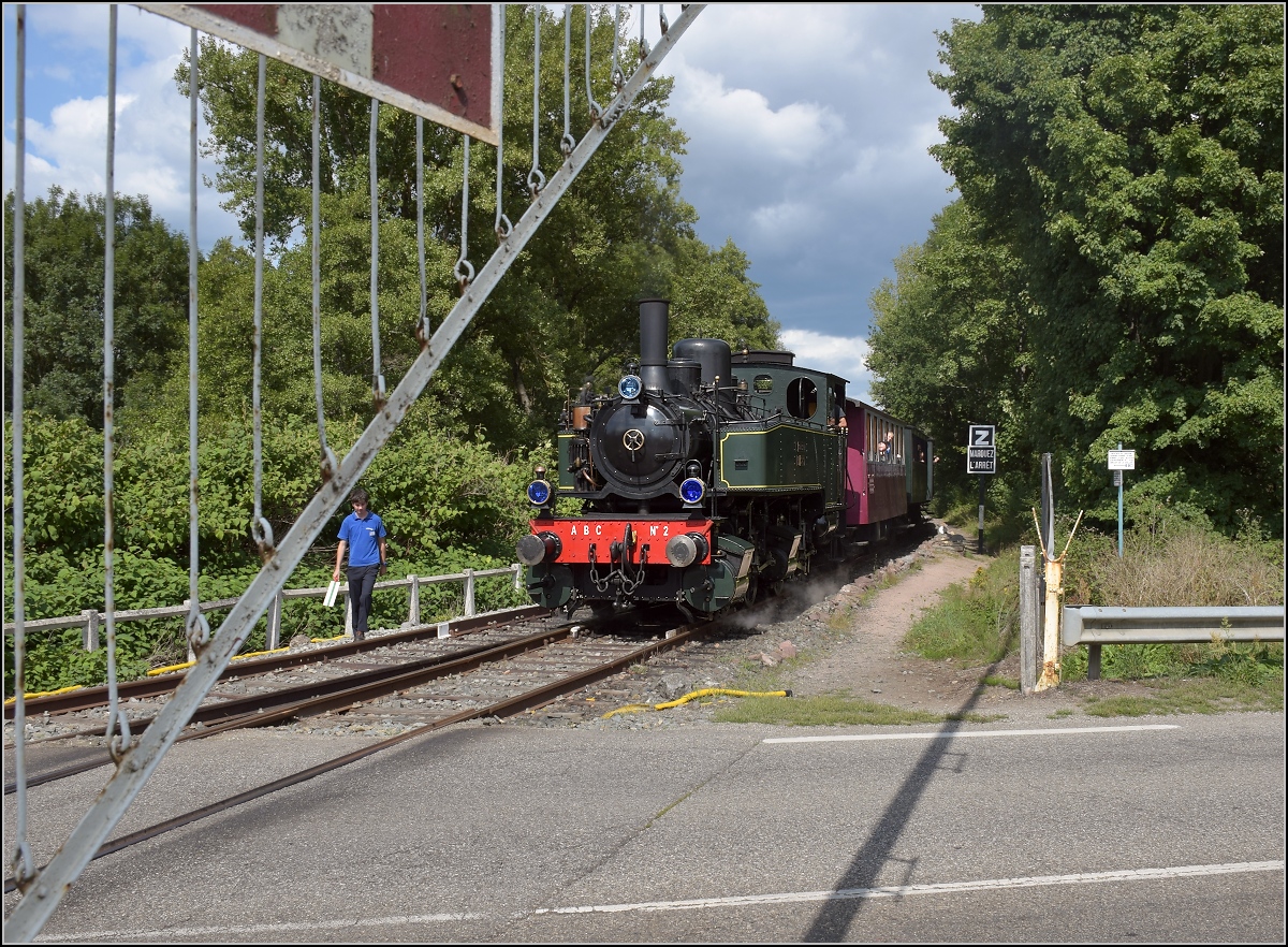Dollertalbahn, ein kaum bekanntes Museumsjuwel.

020+020T système Mallet n° 10416 muss vor der Querung der Straße nach Masevaux anhalten, damit man sicher rüberkommt. Ein wenig gewöhnugsbedürftig ist dabei schon, dass die Lok am Straßenrand dräut, während noch die Schranken runtergelassen werden. Dieser Vorgang, mal mit Kurbeln, mal mit technischer Hilfe erscheint den Augen doch ein wenig seltsam. Burnhaupt, August 2017.