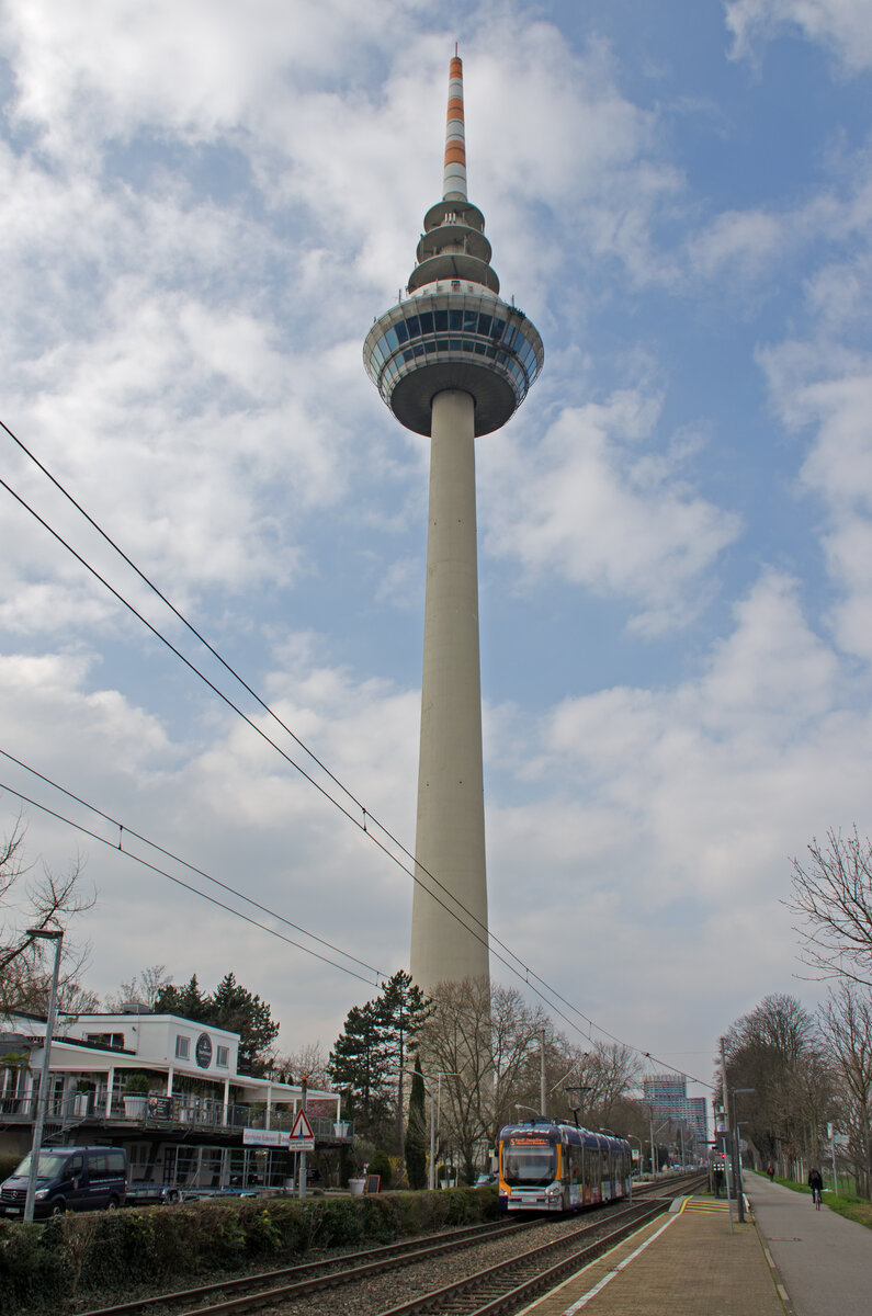 Donnerstag den 07.03.2024 um 13:32 Uhr in Mannheim. Der Mannheimer Fernmeldeturm hat eine Gesamthöhe von 218 Meter. Die Aussichtsplattform (untere Fensterreihe) befindet sich auf 121 Meter. Das Dreh-Restaurant (obere Fensterreihe) befindet sich auf 125 Meter. Der Turm befindet sich beim Luisenpark am Neckar. Der Fernmeldeturm wurde 1975 zur Bundesgartenschau eröffnet. Am Fernmeldeturm befindet sich die Bus- und Strassenbahnhaltestelle  Fernmeldeturm“. Strassenbahnlinie Nr. 5 und Buslinie Nr. 60 führen beide vom Hauptbahnhof zum Fernmeldeturm. Die vorbeifahrende Strassenbahn trägt die Werbung für die Polizei. Hierbei wirbt die Strassenbahn für den Nachwuchs bei der Polizei. Koordinaten GMS (Grad, Minuten, Sekunden): N 49° 29’ 12.0’’ O 8° 29’ 39.2’