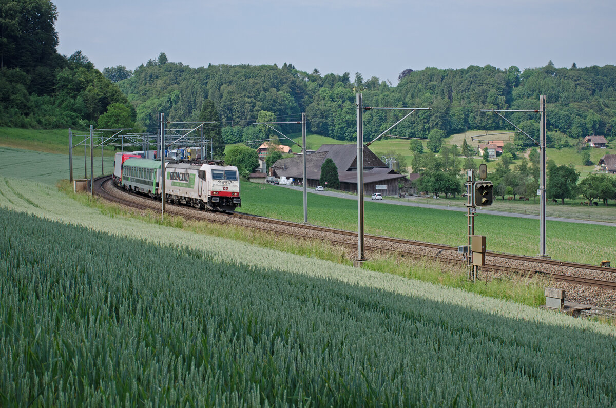 Donnerstag den 08.06.2023 um 10:12 Uhr auf der Strecke zwischen Burgdorf und Wynigen zwischen den Weilern Grafeschüre / Grafenscheuren und Stöckacher / Stockacker auf der Höhe von Räckholter fährt soeben ein RoLa-Zug (Zugnummer konnte für diesen Zug von mir heute leider nicht ermittelt werden) durch. Dieser Zug verkehrt von Novara (I) über Domodossola – Brig – Thun – Bern – Olten – Basel nach Freiburg im Breisgau (D). RoLa bedeutet  Rollende Autobahn“: komplette Lastwagen werden an speziellen Terminals auf den Zug verladen und die Fahrer reisen in einem Begleitwagen mit. Zuglok ist die 91 83 2186 909-4 I-BLSC (Frontbezeichnung 186 909). Die Lok trägt ein Wappen mit der Anschrift  Monte Olimpino“ was auf die Ortschaft Monte Olimpino hinweist. Dieser Ort befindet sich zwischen Chiasso und Como. Lokhersteller: Bombardier. Typ: TRAXX F140 MS. Fabriknummer: 34370. Baujahr: 2008. Der Begleitwagen für die LKW-Fahrer ist der Bcm 61 85 5900 100-2 CH-RALP. Dieser Wagen ist Klimatisiert. Etwas Vorhalt auf dem Bild um die schöne Landschaft zu zeigen schadet sicher nicht. Koordinaten GMS (Grad, Minuten, Sekunden): N 47° 4’ 38.5’’ O 7° 38’ 34.9’’