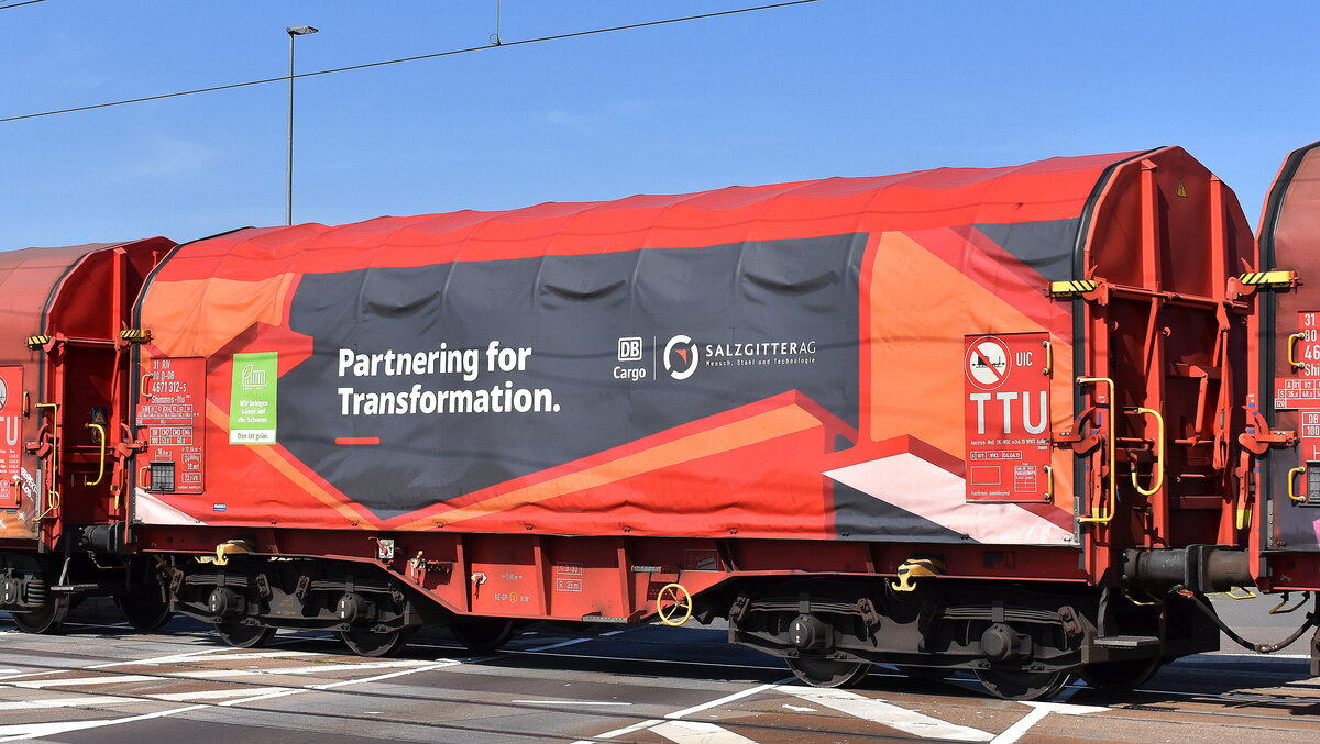 Drehgestellflachwagen mit vier Radsätzen, verschiebbarem Planenverdeck und Lademulden für Coil-/Spaltbandtransporte der DB Cargo mit interessanter Werbung auf der Plane mit der Nr. 31 RIV 80 D-DB 4671 312-5 Shimmns-ttu 723.4 in einem gemischten Güterzug am 02.09.24 Höhe Bahnhof Rodleben.