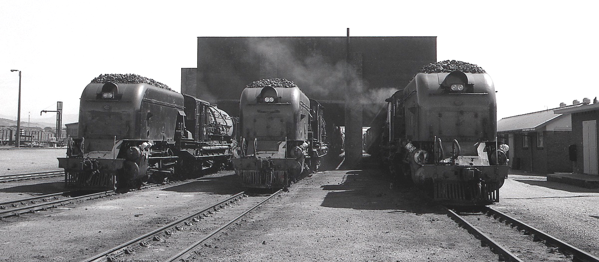 Drei Beyer-Garrrats der Reihe GMAM stehen im November 1976 im Depot Voorbaai der SAR. Bei diesen Lokomotiven sind zwei Triebwerkseinheiten durch einen Brückenrahmen, auf dem Kessel und Führerhaus untergebracht sind, verbunden. Zum Zeitpunkt der Aufnahme war die Strecke Mosselbaai - George - Oudshoorn noch fest in der Hand dieser imposanten Lokomotiven. 