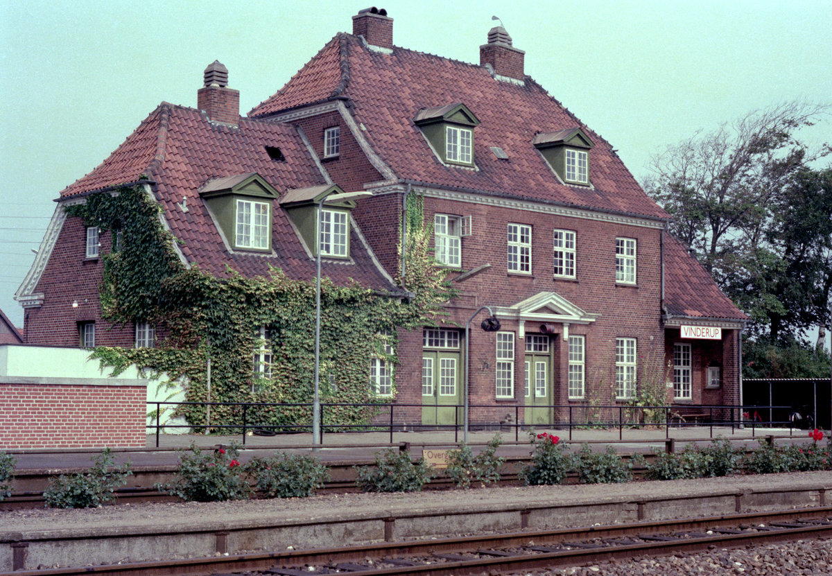 DSB Bahnhof Vinderup am 5. September 1976. - Der Bahnhof, der sich an der Bahnstrecke Langå - Struer befindet, und der heute von ARRIVA-Triebzügen bedient wird, wurde 1915 vom damaligen Chefarchitekten der DSB, Heinrich Wenck (1851 - 1936), entworfen. Der Architekt (und Kunstmaler) Heinrich Wenck spielt eine sehr große Rolle innerhalb der dänischen Bahnarchitektur, da er eine ganze Reihe von dänischen Bahnhofsgebaüden entworfen hat. - (Neuer) Scan eines Farbnegativs. Film: Kodak Kodacolor II. Kamera: Minolta SRT-101. 