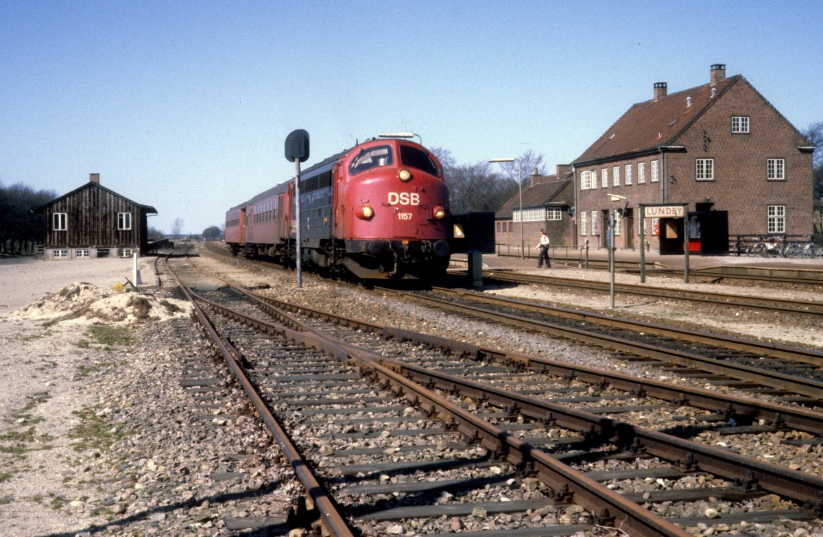 DSB-Kleinstadtbahnhöfe: Bahnhof Lundby am 14. April 1981. Das Bahnhofsgebäude rechts im Bild ersetzte 1926-27 das ursprüngliche Gebäude, das zur Zeit der Aufnahme noch existierte. - Am Bahnsteig hält ein Personenzug bestehend aus der Diesellok My 1157 und Personenwagen. Der Zug fährt in Richtung Vordingborg.