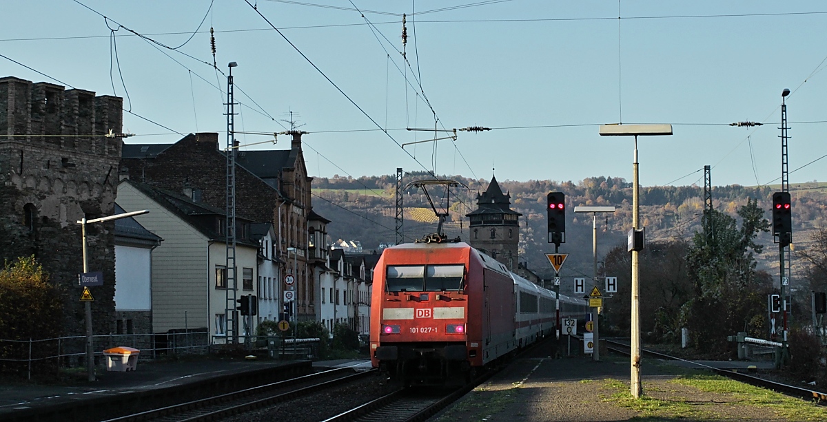 Durch eine Gebäudelücke fällt noch ein schmaler Sonnenstrahl auf 101 027-1, die am 16.11.2018 kurz vor 15.00 Uhr den Bahnhof Oberwesel durchfährt