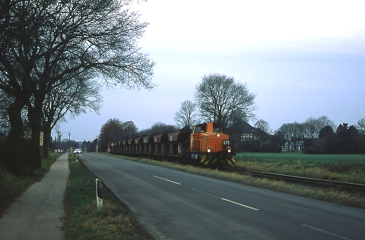 Durch die typisch niederrheinische Landschaft bei typisch niederrheinischem Dezemberwetter befördert RBH 575 (Kraus-Maffei M700C 1973) am 20.12.2012 einen Kohlezug zum Übergabebahnhof in Moers. 