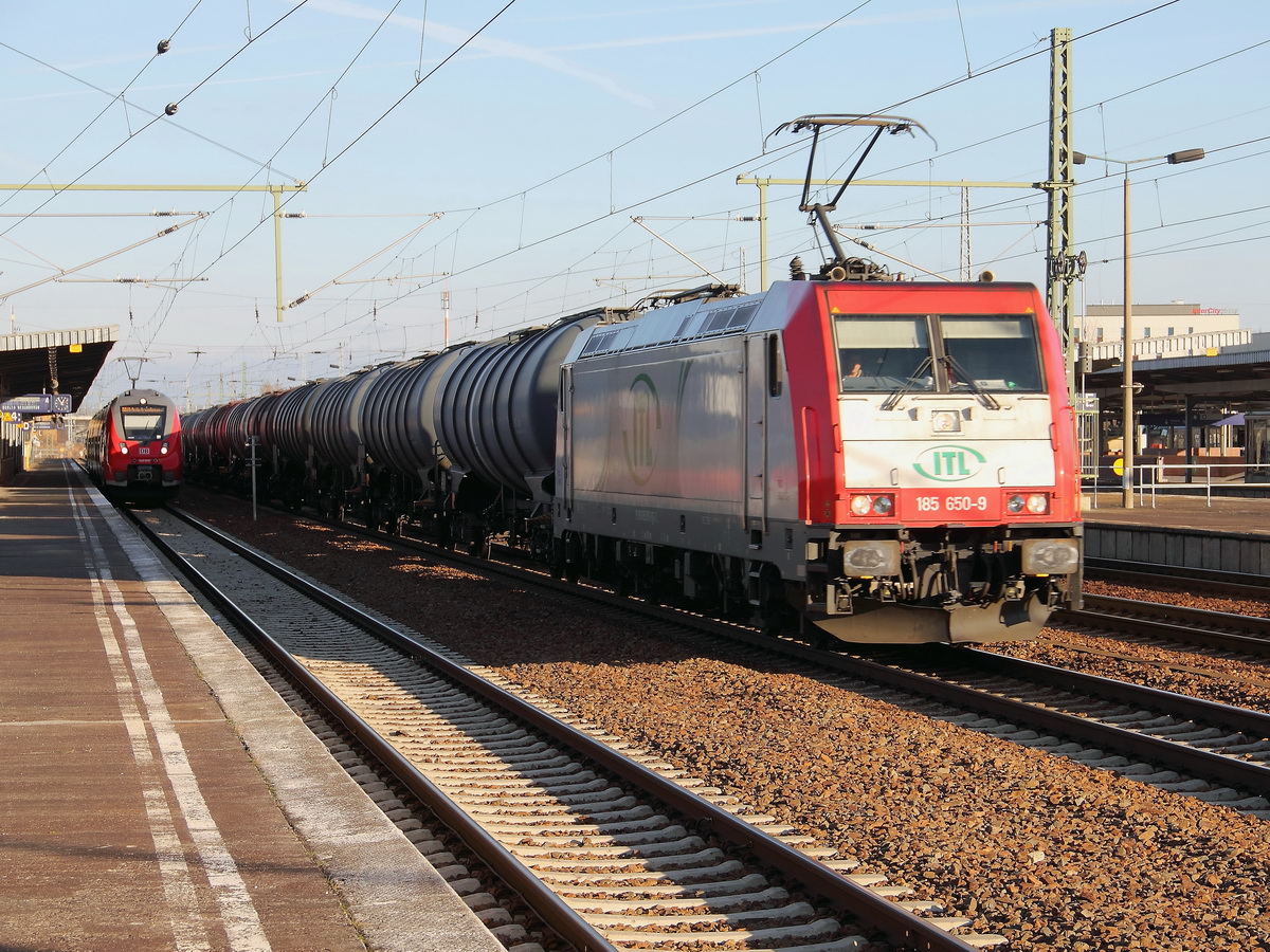 Durchfahrt 185 650-9 der  durch die ITL - Eisenbahngesellschaft mbH gemietete E-Lok mit einem Ganzzug Kesselzug  umweltgefährdender Stoffe (UN Nummer 1203, Gefahrenzahl 33) am  27. Dezember 2013 durch den Bahnhof Berlin Schönefeld Flughafen. 
Im Hintergrund 442 828 mit 442 328 als RB 19 nach Berlin Gesundbrunnen auf Gleis 4.

