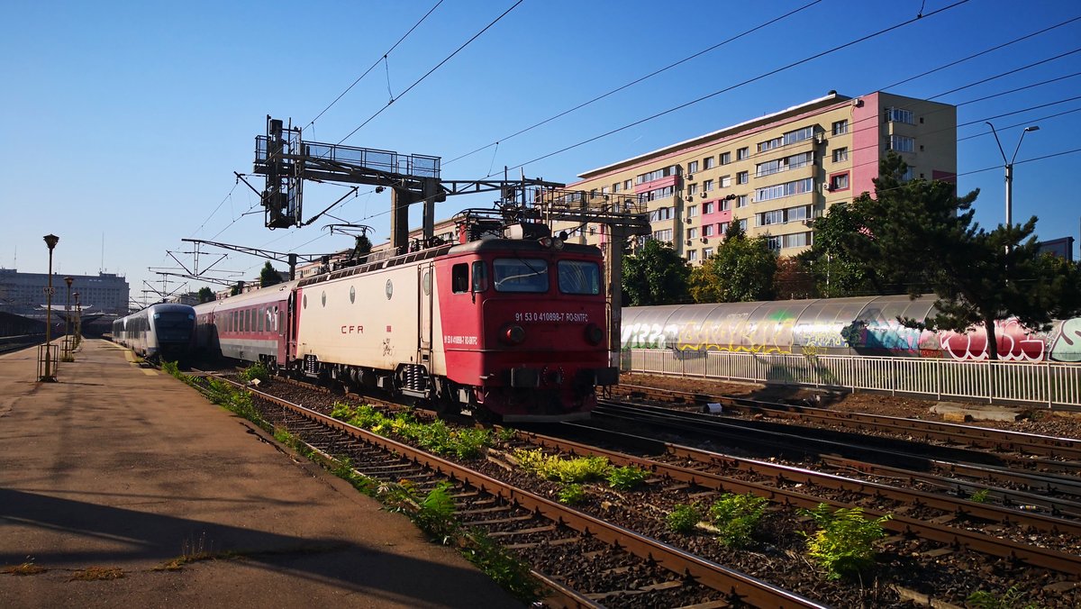 E-Lok 91-53-0-410898-7 mit IR in Richtung Targu Jiu am 13.08.2018 im Nordbahhof Bukarest. Daneben wartet eine Garnitur bestehend aus zwei Triebzügen der Baureihe 96 auf grünem Licht um in den Betriebswerk zurückzukehren.