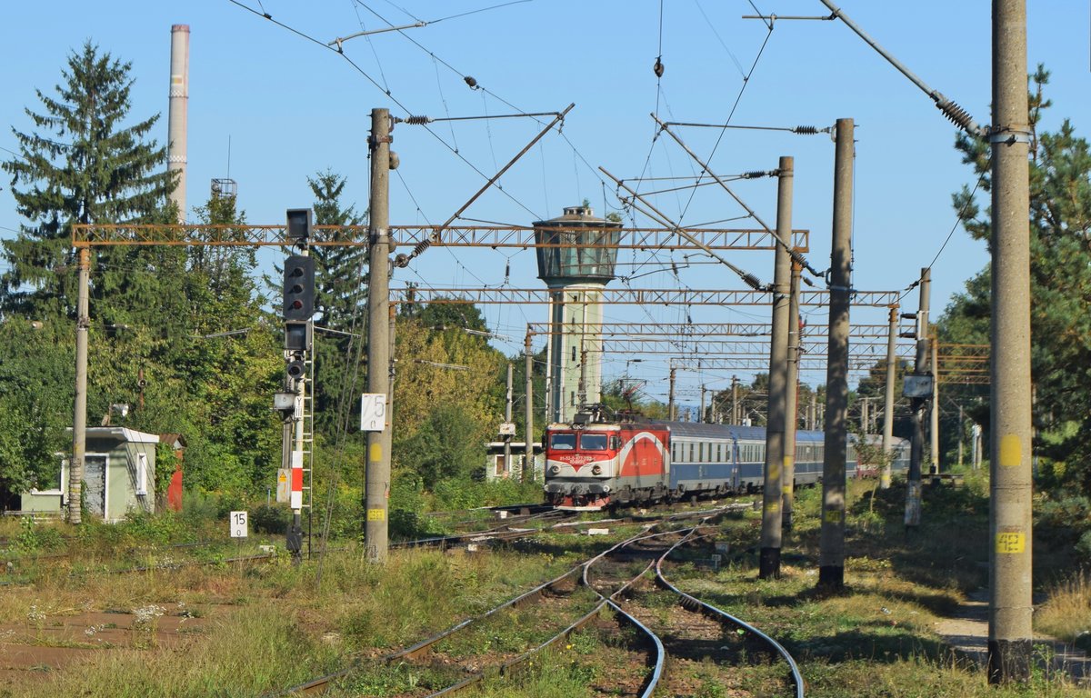 E-Lok 91-53-0-477753-4 zieht am 15.09.2017 mit internationaler Garnitur von Bukarest nach Budapest in Bahnhof Brasov ein. Im Hintergrund ist der Wasserturm des Bahnhofs Brasov zu sehen.