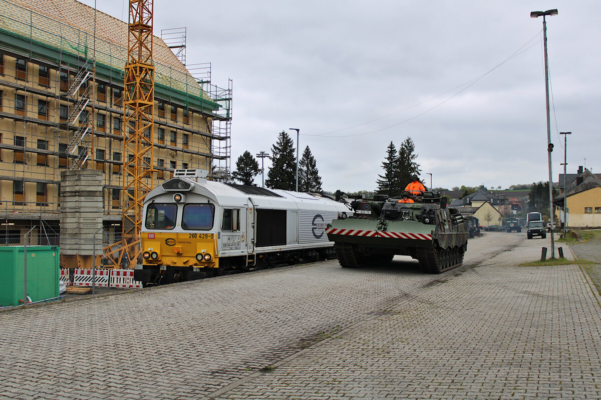 ECR 266 429-0 steht neben einem Bundeswehr Panzer, welcher nach erfolgter Beladung des Zuges wieder in die Kaserne zurück fährt. Die Lok rangiert nun die Wagen an den restlichen Zugteil. (29.04.2023)