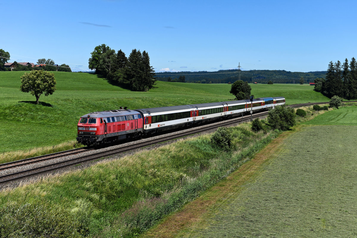 Eigentlich ein klassisches Beispiel dafür, dass die Kamera im Hochsommer um die Mittagszeit besser eingepackt bleibt. Nachdem die Zeit der dieselbespannten EuroCities im Allgäu aber unweigerlich abläuft, war mir der EC 194 auch zur absoluten Hochlicht-Phase ein Bild wert. Entstanden ist die Aufnahme bei Görwangs, es führte die Mühldorfer 218 422. 