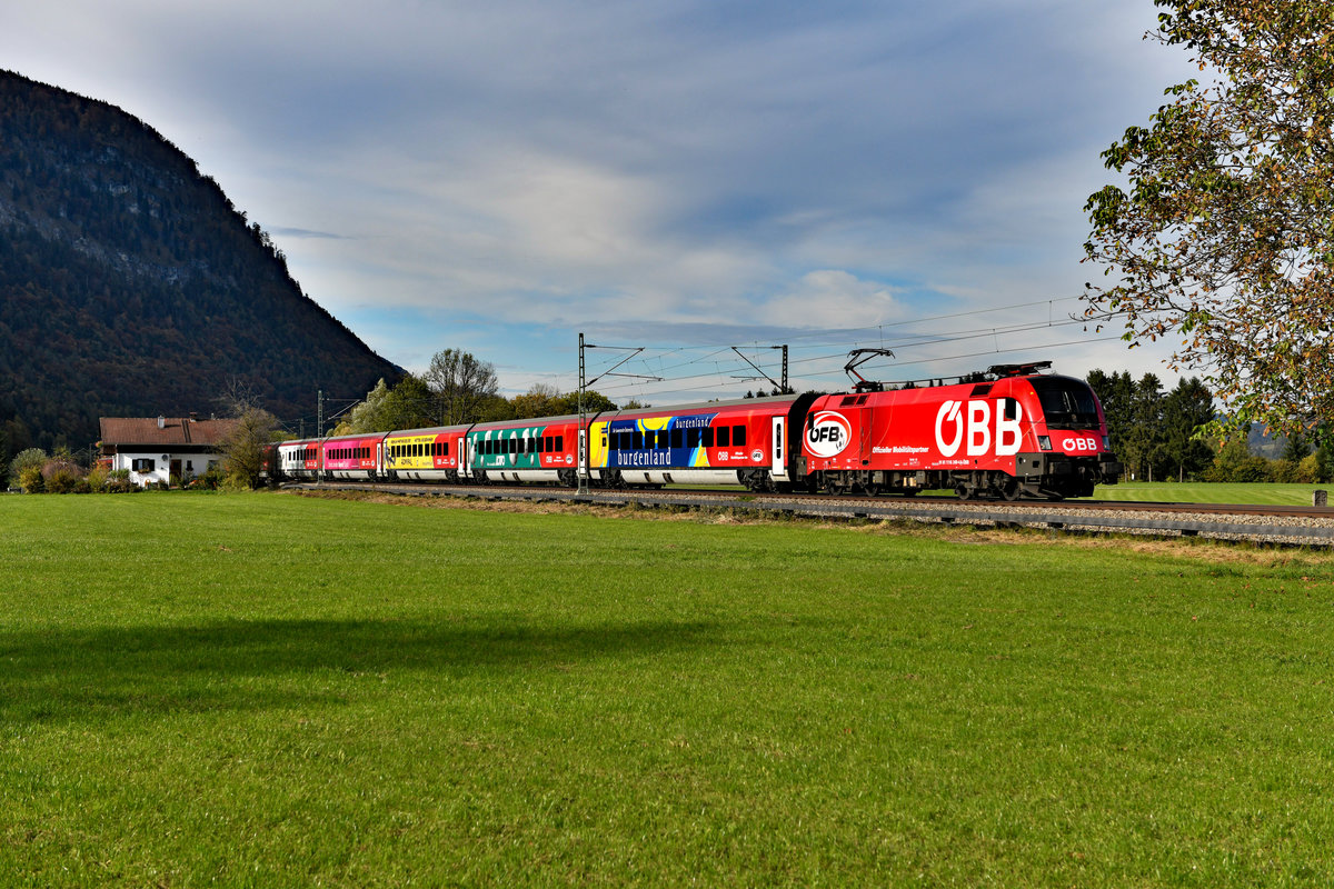 Eigentlich wollte ich mir den zum Aufnahmezeitpunkt gerade erst neu gestalteten ÖFB-Railjet nur ansehen, denn am Nachmittag des 18. Oktober 2019 waren bereits die ersten Ausläufer einer Schlechtwetterfront aufgezogen. Als die 1116.249 mit ihrem bunten Wagenpark als RJX 564 von Flughafen Wien Bahnhof nach Innsbruck HBF in Niederaudorf durchkam, lugte die Sonne nochmals kurz durch die Wolkendecke und es ergab sich diese interessante Wetterstimmung. Aktuell ist dies übrigens die einzige Railjet-Garnitur mit Komplettwerbung. Die  längste Flagge Österreichs  und der  Ski Austria  wurden entklebt. Bemerkenswert, dass die bereits sehr ähnlich gestaltete 1116.225 ihr  ÖFB -Design gegen eine ÖBB-Werbung tauschen musste, wohingegen die abgebildete 1116.249 neu foliert wurde. 