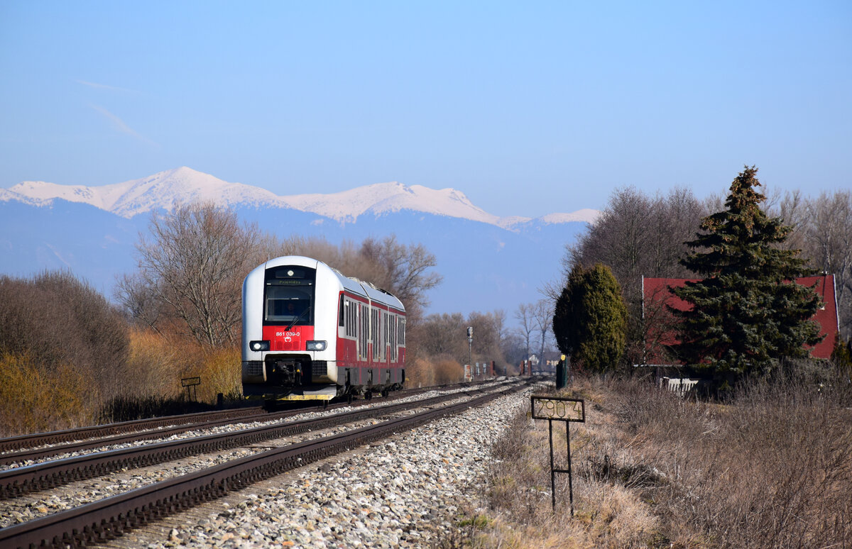 Ein 861-er Triebzug ist unterwegs von Vrútky (Rutteck) nach Horná Štubňa kurz vor Blažovce. 
Über dem Zug sieht man die schneebedeckte Fátra.
Blažovce, 04.03.2023.