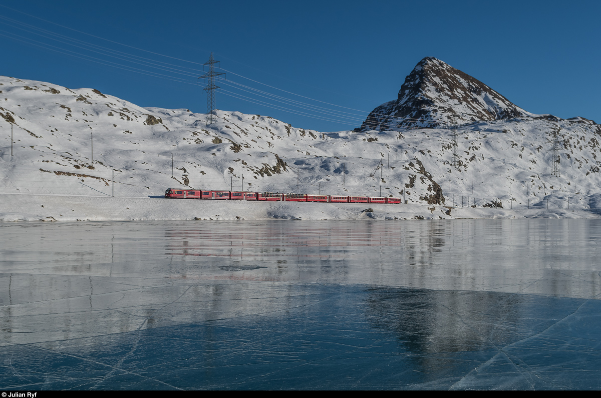 Ein Allegra fährt am 29. Dezember 2016 mit dem Regio 1644 Tirano - St. Moritz dem mit Schwarzeis bedeckten Lago Bianco entlang. Dahinter erhebt sich der 2599 Meter hohe Piz Campasc.