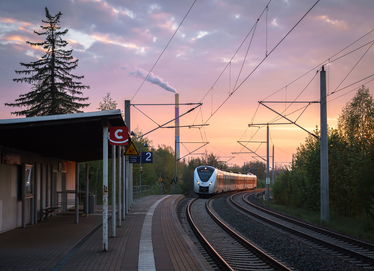 Ein Alstom Coradia Continental-Triebzug der Mitteldeutschen Regiobahn durchfährt am Abend des 01. Mai 2019 den Haltepunkt Chemnitz-Hilbersdorf als RE 3 nach Dresden Hbf. Im Hintergrund ist der Schornstein des Heizkraftwerks Chemnitz-Nord zu sehen.