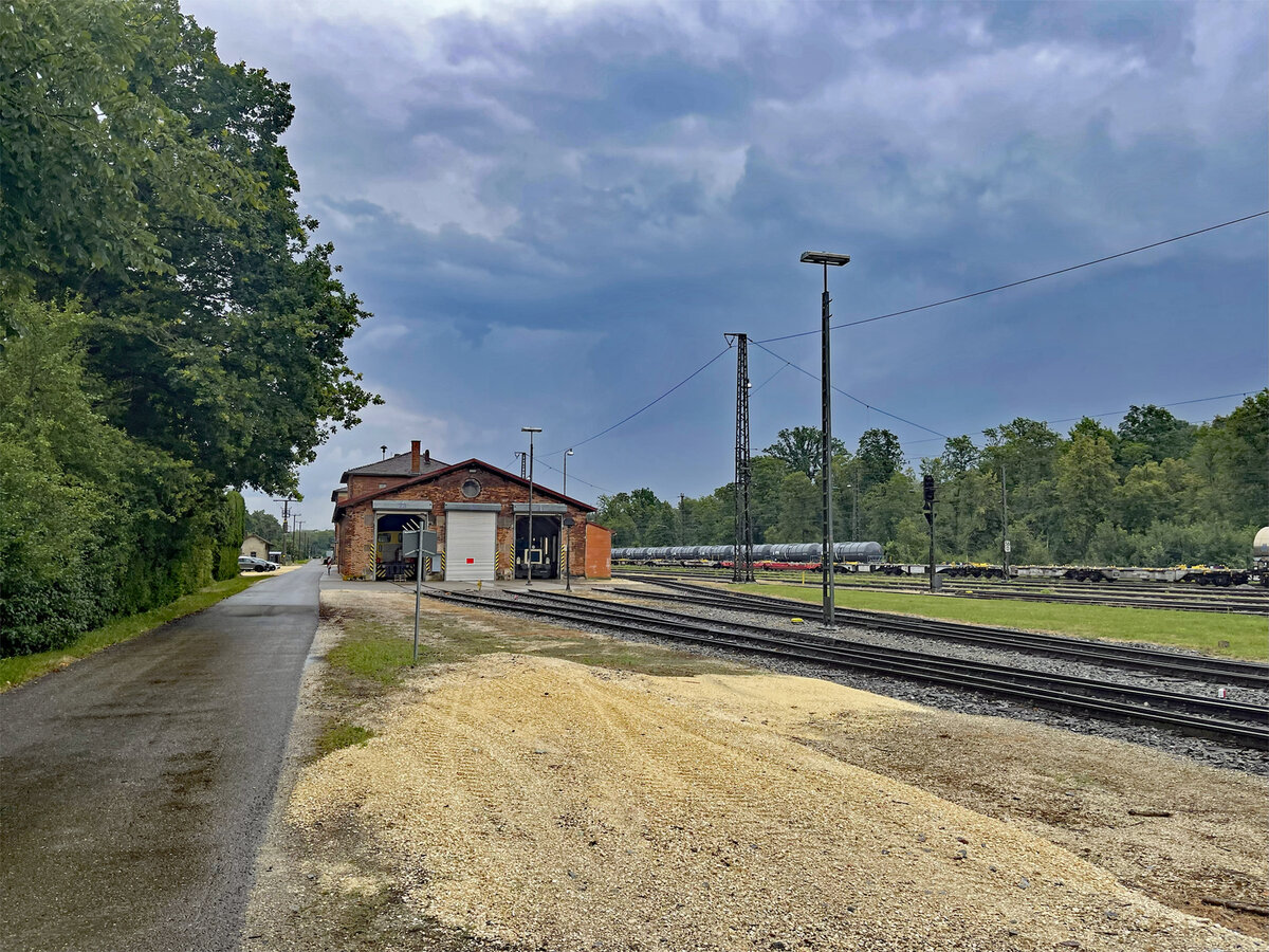 Ein Blick auf das Gelände des unter Denkmalschutz stehenden ehemaligen Bahnhofsgebäudes Neuoffingen mit dem dreiständigen Lokschuppen, aufgenommen am 15.07.2025. Ein Teil der Anlage mit mehreren Nebengleisen wird inzwischen von der NFG Bahnservice betrieben (Quelle: Wikipedia)