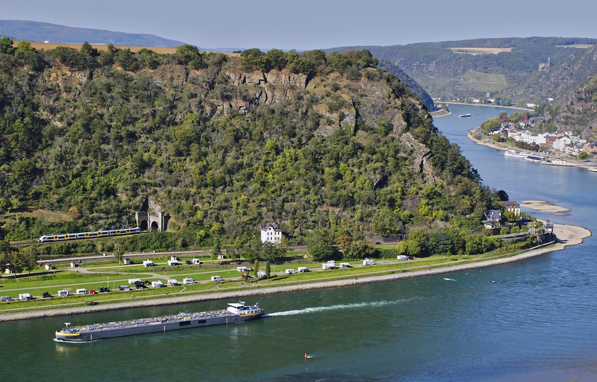 Ein Blick vom Loreleyfelsen auf die linke Rheinstrecke: Am 11.10.2023 wird ein 460 der Mittelrheinbahn auf dem Weg von Mainz nach Koblenz gleich in den Banktunnel einfahren. Die Wohnmobile auf dem Campingplatz dürften in der Mehrzahl gelbe Nummernschider haben...