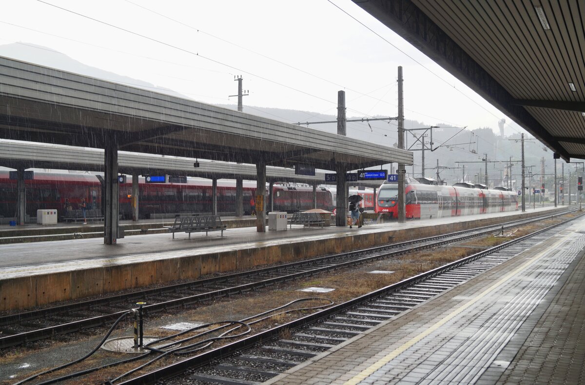 Ein Blick über den Innsbrucker Hauptbahnhof Richtung Süden während eines starken Sommerregens am Nachmittag des 10.07.2020. Auf Gleis 41 steht der REX zur Fahrt nach Landeck-Zams schon bereit, während der Lokführer noch durch den Regen muss, um seinen Zug zu erreichen...