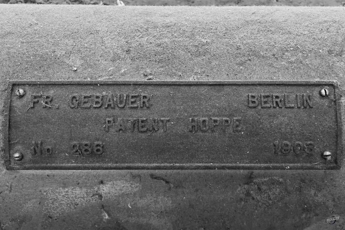 Ein Firmenschild auf dem staubbehaarten Hydraulikstempel von einem der mehr als hundert Jahre alten Prellböcken. (Antwerpen Centraal, Juli 2018)