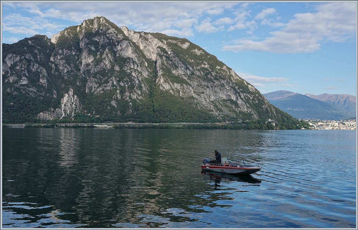 Ein Fischer auf dem Lago di Lugano, der Monte Salvatore und wenn man genau hinschaut, ein ICN auf dem Weg nach Lugano. 
29. Sept. 2018