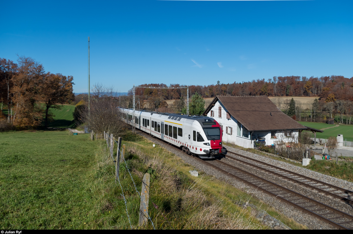 Ein FLIRT der TPF fährt als RE Fribourg - Bulle in der Nähe von Neyruz an einem ehemaligen Bahnwärterhaus vorbei. Auf diesem Streckenabschnitt stehen derzeit noch alte Fahrleitungsmasten, das Fundament für die neuen ist jedoch bereits gemacht.
07.11.2015