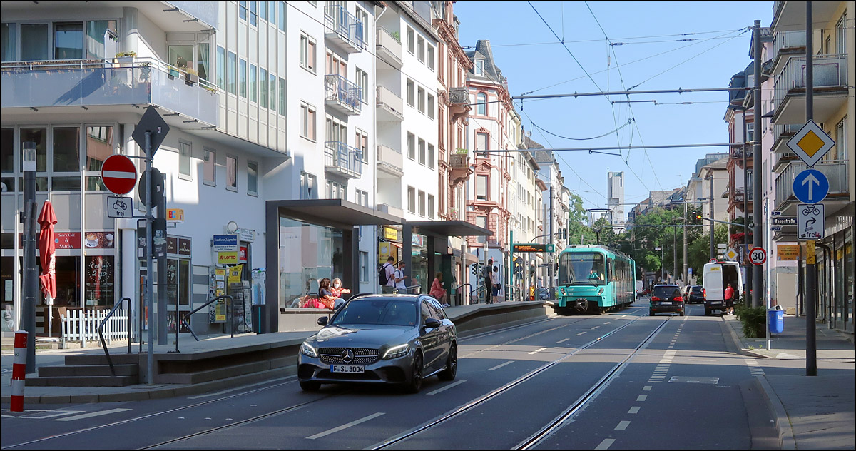 Ein Fremdkörper im Frankfurter 'U-Bahnnetz' -

Obwohl meist als U-Bahn bezeichnet, handelt es sich beim Frankfurter Netz um ein 'Stadtbahn', da eine echte U-Bahn ausschließlich kreuzungsfrei (Unabhängig) unterwegs ist. In Frankfurt gibt es zahlreiche oberirdische Abschnitte mit eigenen Bahnkörpern aber mit vielen Kreuzungen durch Individualverkehr und Fußgänger. Und nur hier in der Eckenheimer Landstraße muss die 'U-Bahn' auf den Fahrspuren des Autoverkehrs fahren.

Hier erreicht gerade ein Stadtbahnzug der Linie U5 in Fahrtrichtung Hauptbahnhof die Haltestelle 'Musterschule'. Die Bahnsteige beider Haltestellen wurden aus Platzgründen versetzt zueinander angeordnet.

21.07.2021 (M)

