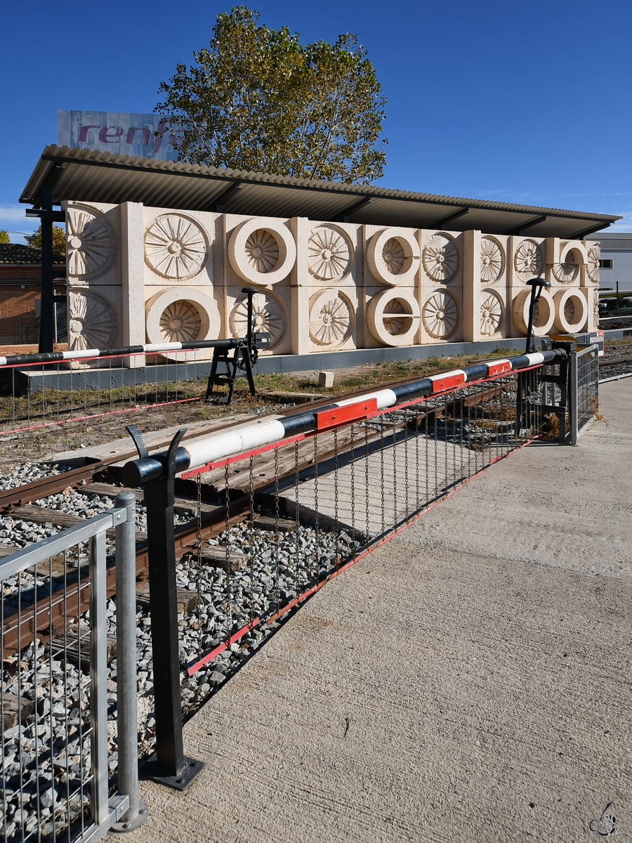 Ein geschlossener Bahnübergang und eine von Radsätzen inspirierte Betonwand, so gesehen im November 2022 auf dem Außengelände im Eisenbahnmuseum von Katalonien.