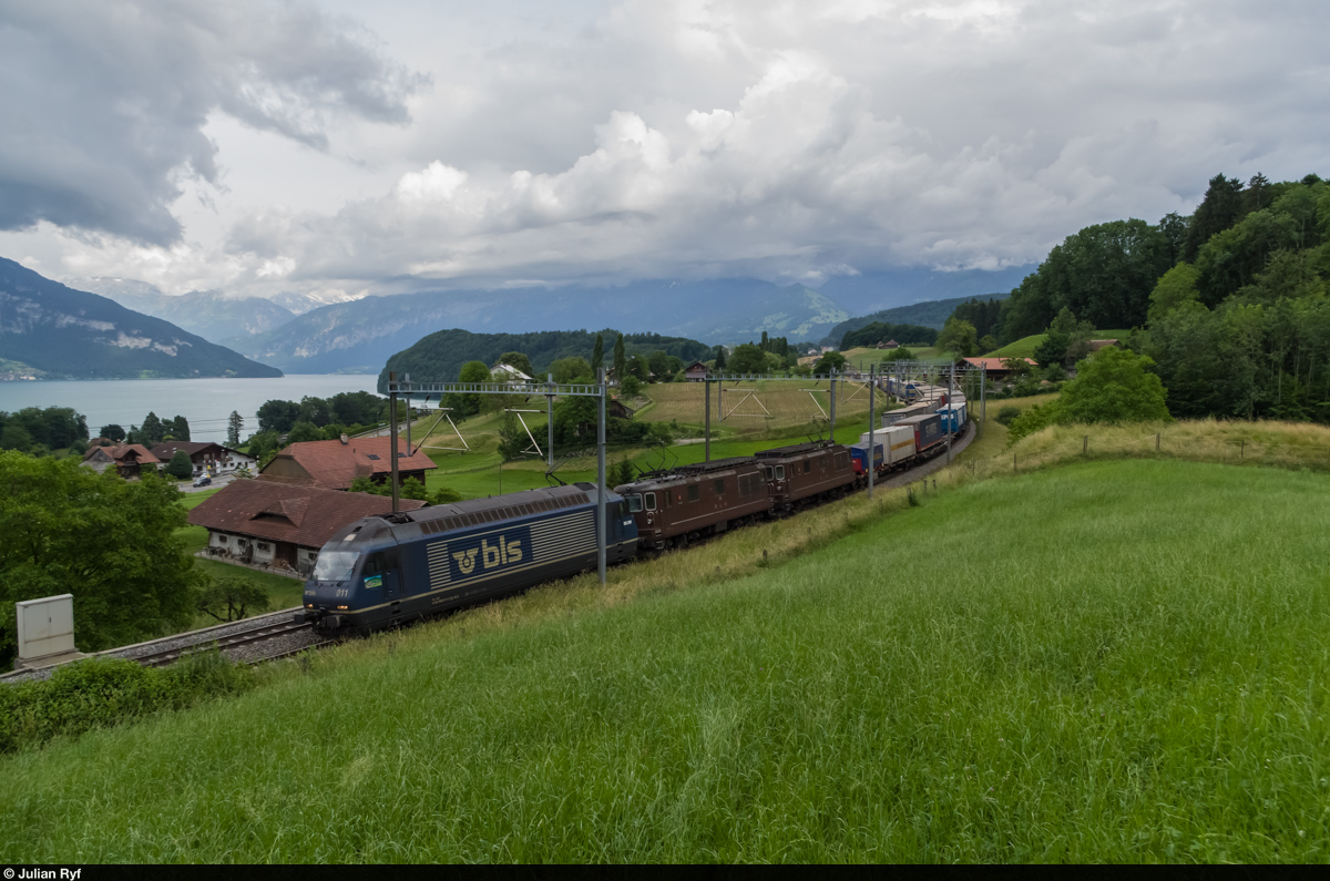 Ein Güterzug von BLS Cargo bespannt mit Re 465 011 sowie zwei Re 4/4 kreuzt am 14. Juni 2015 bei Kumm am Thunersee nordwärts fahrend einen Crossrail Güterzug. Die Loks verkehren trotz des relativ grossen Altersunterschiedes (ca. 30 Jahre) in Vielfachsteuerung.