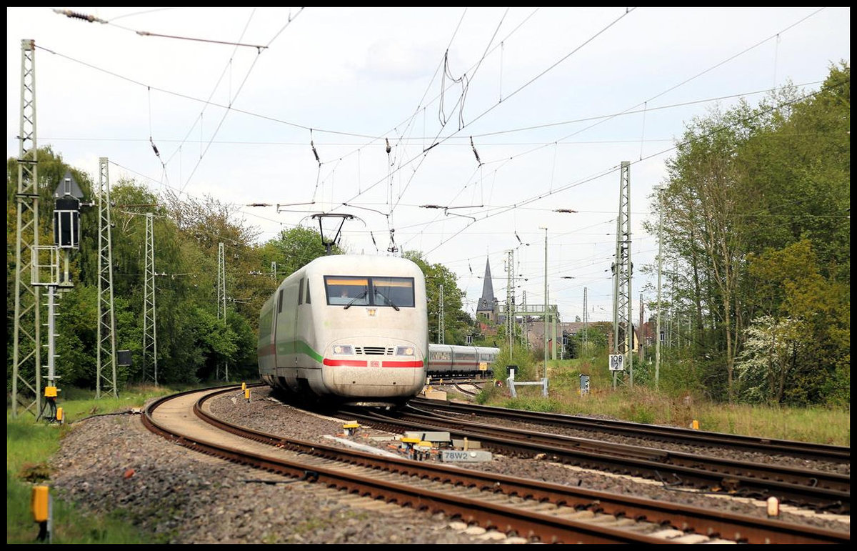 Ein ICE 1 mit grünem Streifen am Motorwagen ist hier auf dem Weg nach Nürnberg und verlässt am 30.4.2020 um 17.40 Uhr gerade den Bahnhofsbereich von Hasbergen. Im Hintergrund ragt die Kirchturmspitze der ev. Kirche über die Szene.
