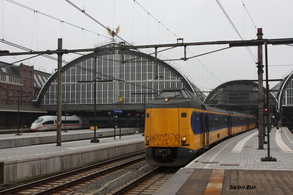 Ein Koploper der NS wartet ebenso wie im Hintergrund ein ICE 3 am 27.10.2014 auf 
Ausfahrt in Amsterdam Centraal. Über allem schmückt das Flügelrad die große Bahnhofshalle.