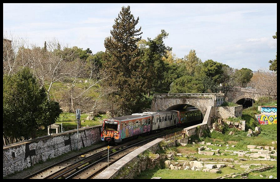 Ein Metro Zug der Linie 1 hat hier am 5.3.2020 gerade den Bahnhof Thissio verlassen und durchfährt antike Brückenbögen, um zum nächsten Bahnhof Monastiraki zu gelangen, der unmittelbar hinter meinem Fotostandort liegt. Leider beschränken sich einige Sprayer nicht nur auf das Verunzieren der Züge und finden offenbar ihr Glück beim Besprühen antiker Kulturstätten. 