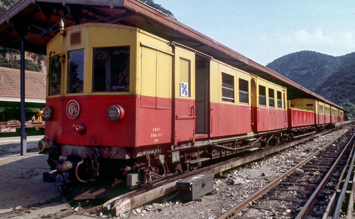 Ein noch komplett im früheren rot/gelben Farbschema lackierter Zug des  Train jaune  mit dem Schmalspur-Triebwagen ZBD 117 in den frühen 1980ern Jahren im Bahnhof Villefranche-de-Conflent. Gut zu erkennen ist auf dem Bild der Stromabnehmer an der von oben abgegriffenen Stromschiene .