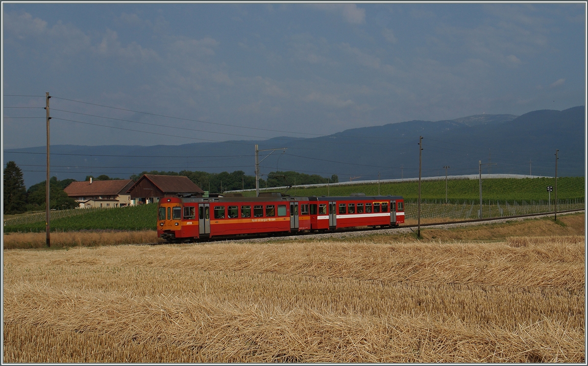 Ein NStCM BDe 4/4 in der  alten  Farbgebung mit seinem bereits umgebauten und umlakierten ABt als Regionalzug 112 auf der Fahrt von Nyon nach La Cure zwischen Les Plantaz und La Vuarpillière am 6. Juli 2015.
