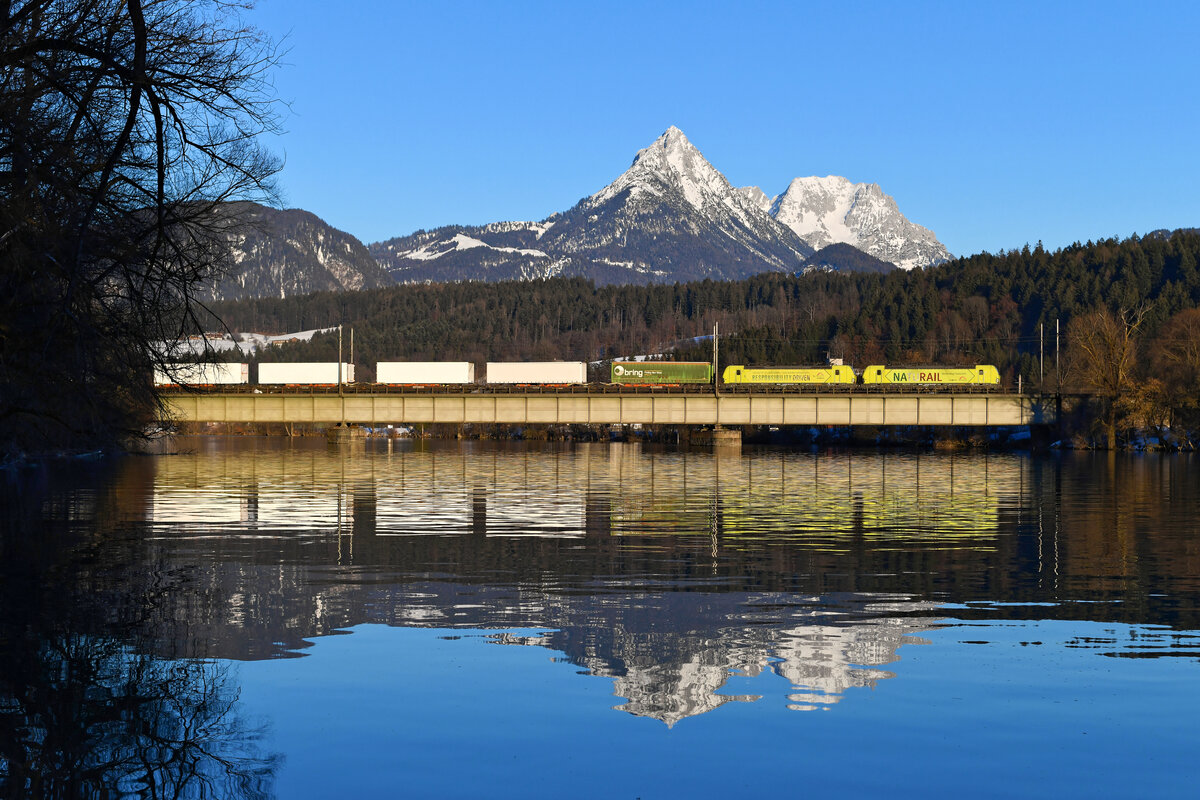 Ein Ruderer hatte kurz vorher Unruhe in die Wasseroberfläche des ruhig dahinfließenden Inns gebracht. Dennoch betätigte ich am späten Nachmittag des 12. Februars 2022 bei der Durchfahrt des DGS 43853 von Rheine nach Puccio Rusco gerne den Auslöser meiner Kamera, wurde der KLV-Zug doch von einem Werbelok-Tandem in Form von 193 559 und 553 bespannt. Die von TXLogistik bei Alpha Trains angemieteten Vectrons weisen auf den umweltfreundlichen Verkehr auf der Schiene hin.  