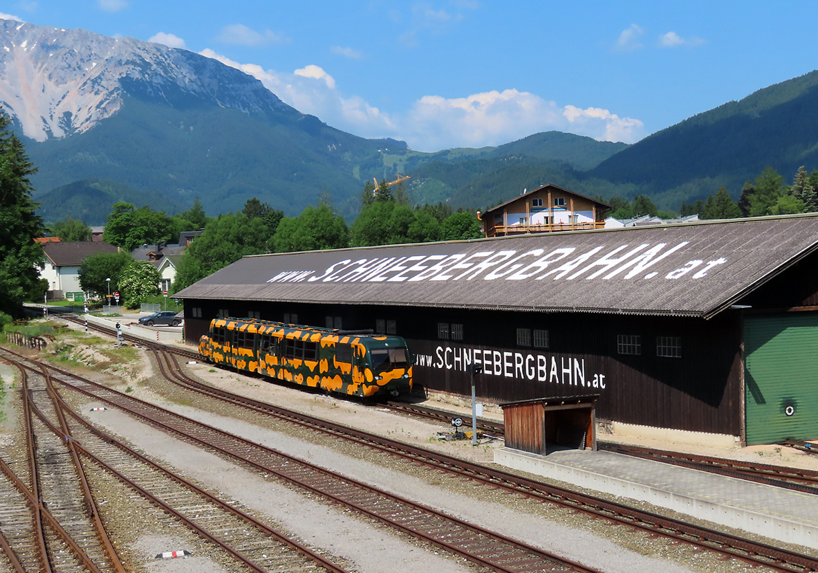 Ein 'Salamander' fährt in den Bahnhof Puchberg am Schneeberg ein. Dieser Dieseltriebzug fährt in 40 Minuten auf den in der linken oberen Ecke sichtbaren Schneeberg (1796 müM). Das Foto wurde von der Aussichtsterrasse gemacht. Puchberg am Schneeberg, 18.6.2023