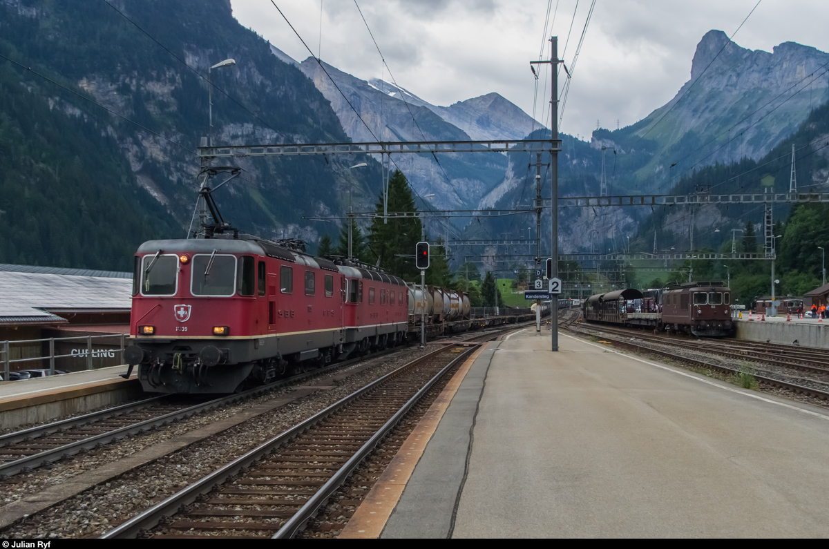 Ein SBB Cargo Güterzug mit Re 10/10 durchfährt am 23. August 2015 den Bahnhof Kandersteg in Richtung Norden. Nebenan steht ein Autoverladezug nach Goppenstein bereit. Im Hintergrund ist der Gemmipass zu sehen.